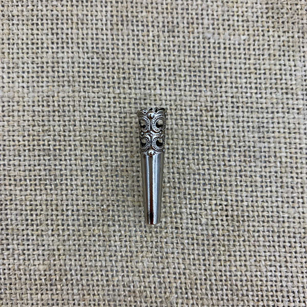 Kleine Trophäenhülse mit filigranem Muster und Nadel für den Hut
