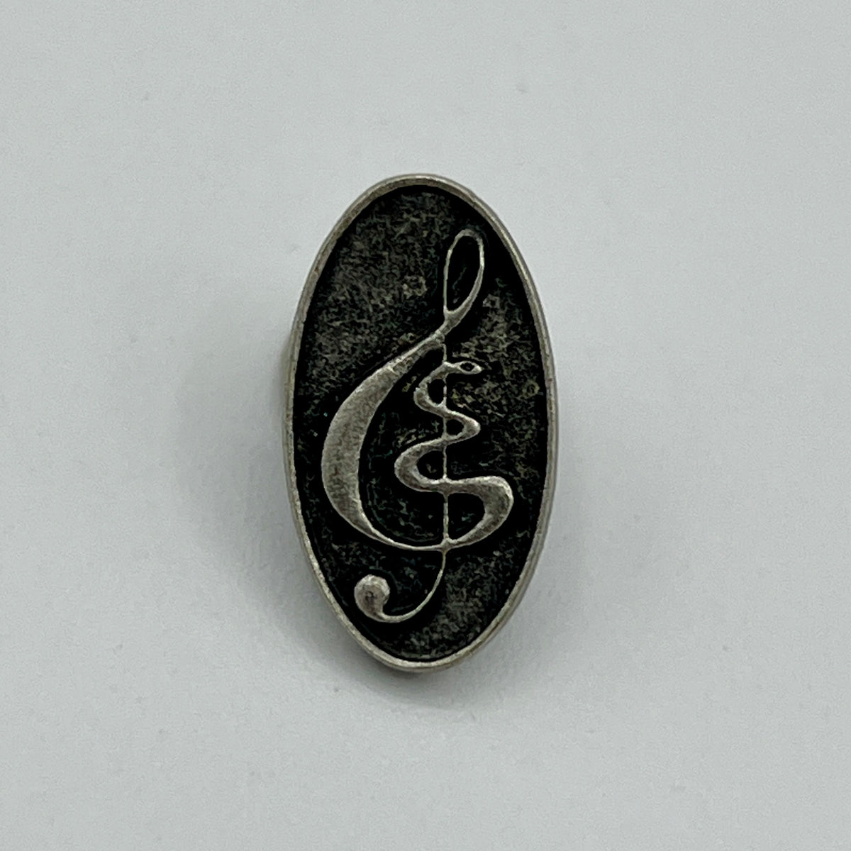 Kleine ovale Anstecknadel mit Notenschlüssel auf schwarzem Grund im Antik-Silber-Look